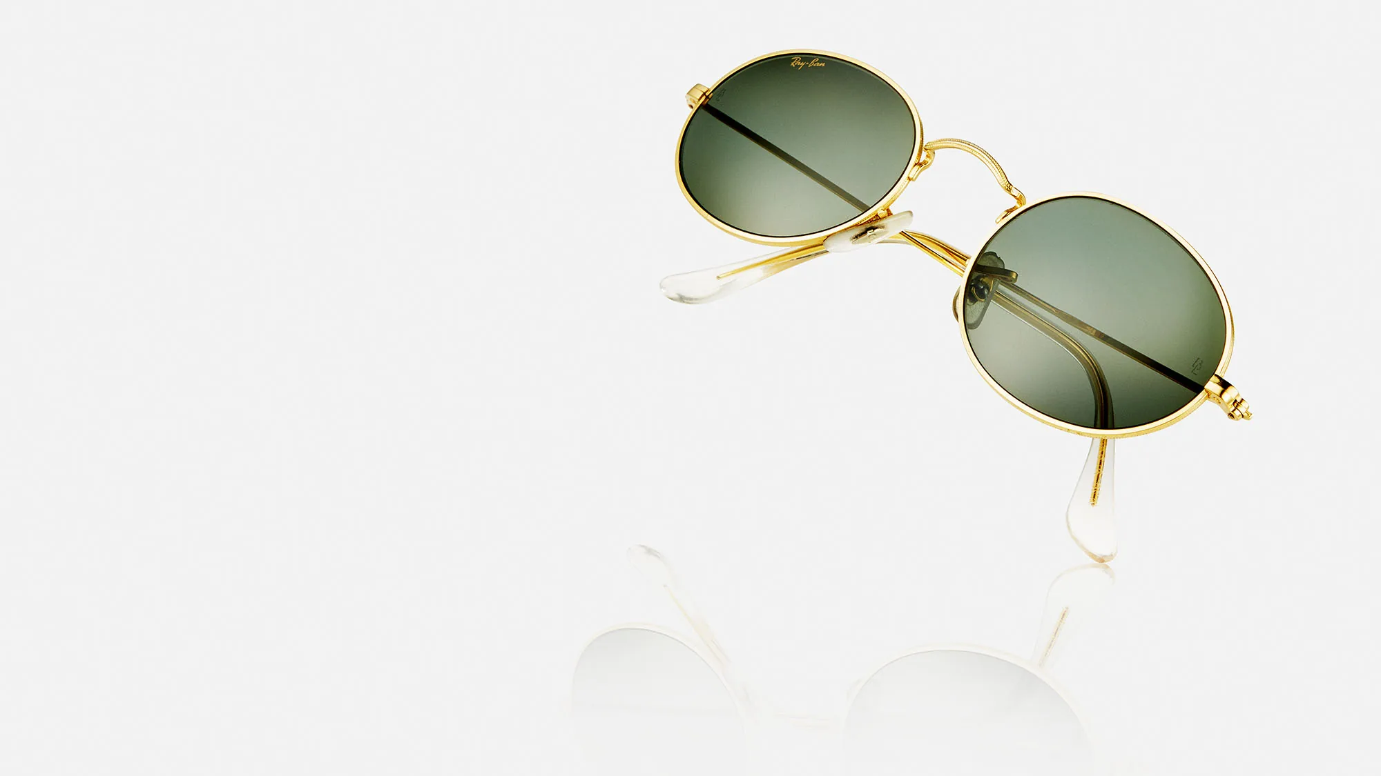 Goldene Sonnenbrille mit grünen Gläsern auf weißem Hintergrund