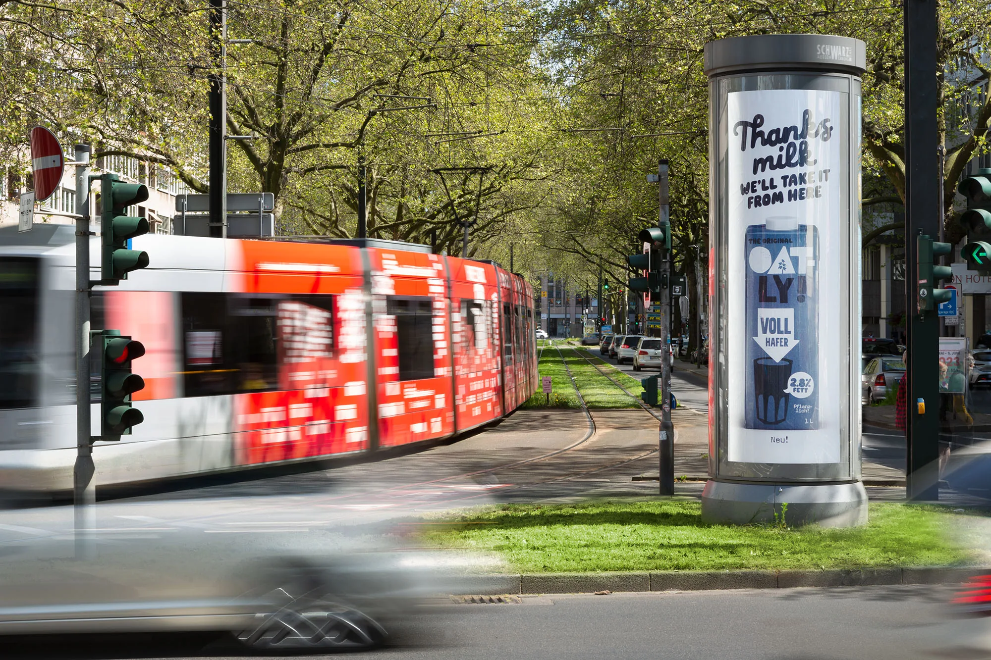 Oatly-Litfaßsäule mit vorbeifahrender Straßenbahn
